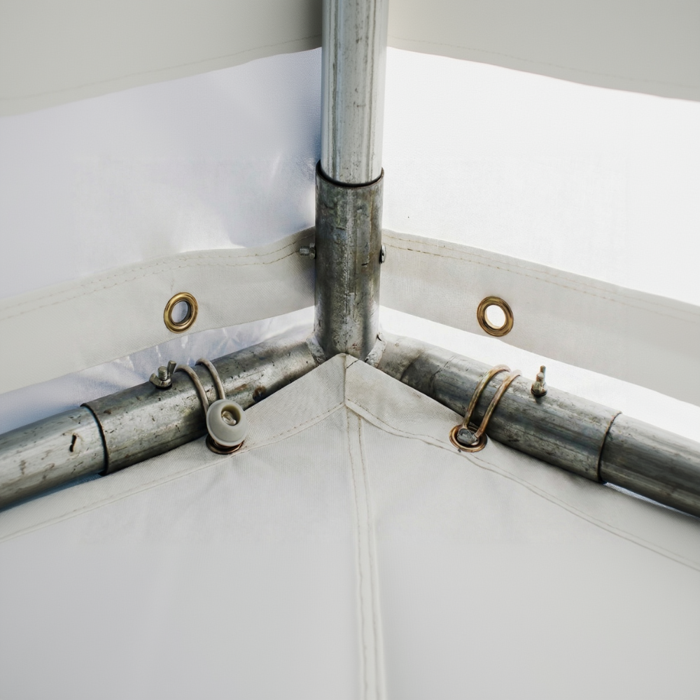 Detailaufnahme der Innenansicht einer Partyzelt-Giebelecke. Das verzinkte Stahlgestänge ist durch Steckverbindungen und Flügelmuttern stabil fixiert. Die weiße Dachplane und die Seitenbahnen sind mit Gummischlaufen durch goldfarbene Metallösen am Rahmen befestigt. Die Planenabschnitte treffen in der Ecke exakt hinter dem Metallgestänge aufeinander.